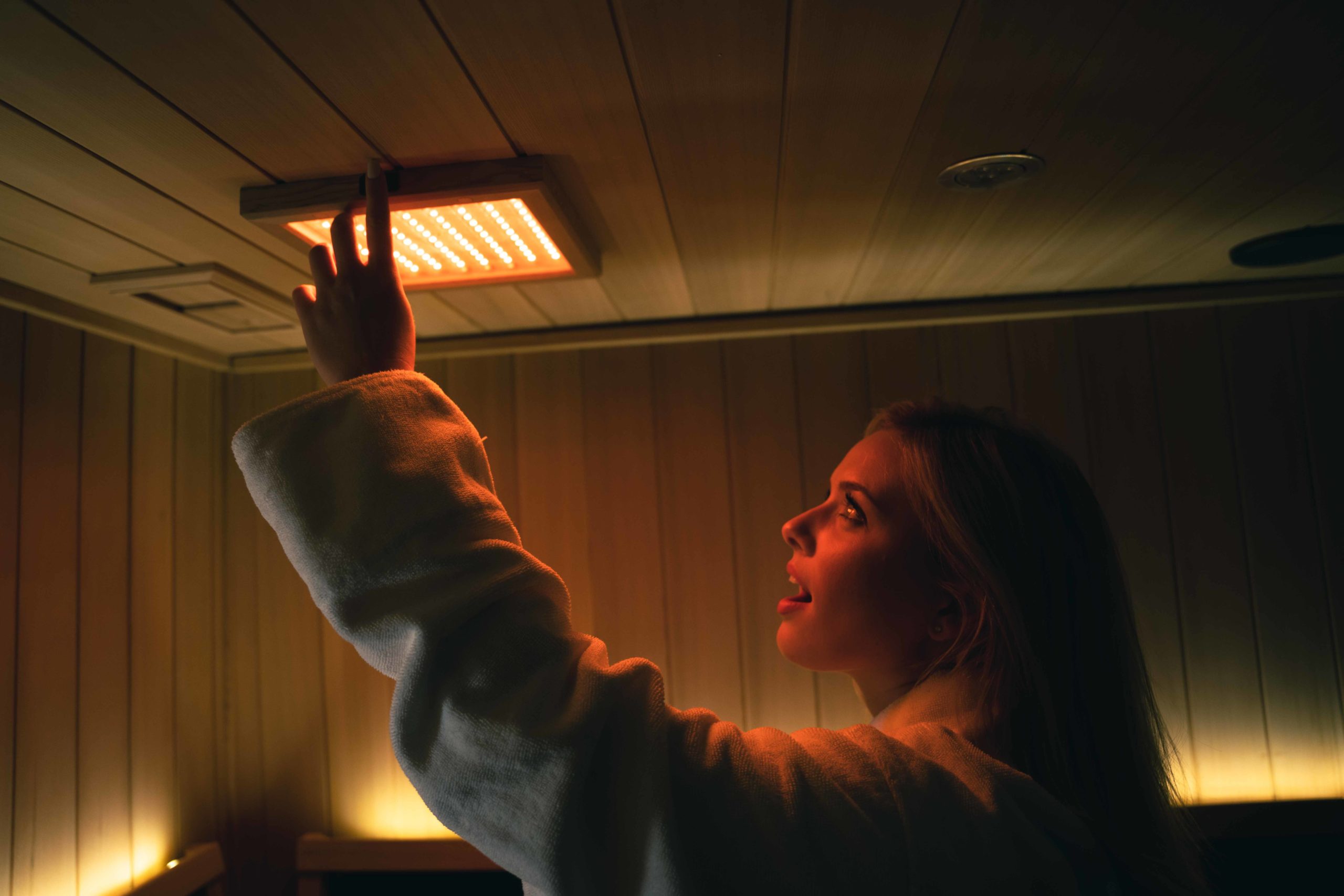 A person in a robe adjusts a glowing light panel on the wooden ceiling in the salon, bathing the room in beautiful, warm ambient lighting. - Tonya Jones SalonSpa| Birmingham, AL