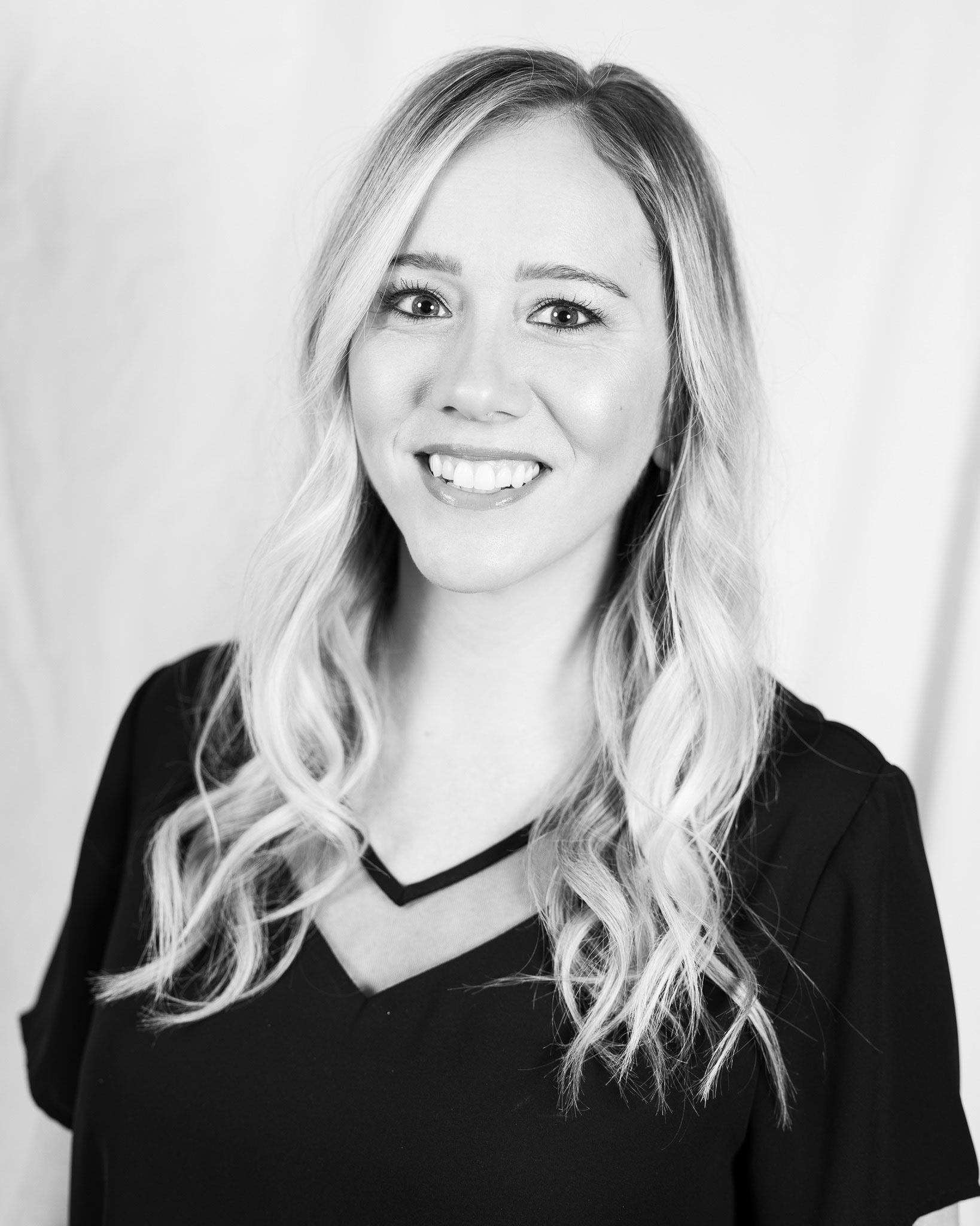 Black and white portrait of a smiling woman with long, wavy hair wearing a V-neck top. - Tonya Jones SalonSpa| Birmingham, AL