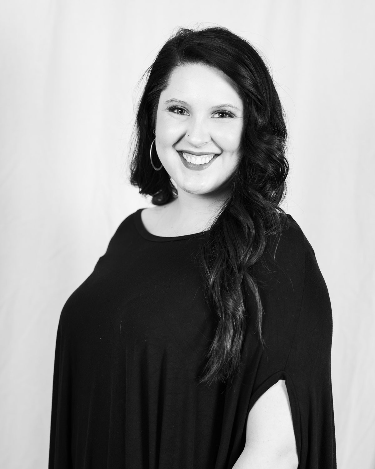 A woman with long dark hair, wearing a black top, smiles at the camera against a plain backdrop. - Tonya Jones SalonSpa| Birmingham, AL