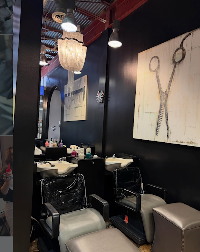 Two black salon chairs face white washbasins in a hair salon with black walls, a chandelier, and artwork featuring scissors hanging above the stations. - Tonya Jones SalonSpa| Birmingham, AL